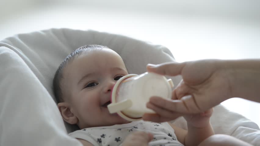 adorable-one-year-old-baby-drinking-milk-from-bottle-fed-by-mother