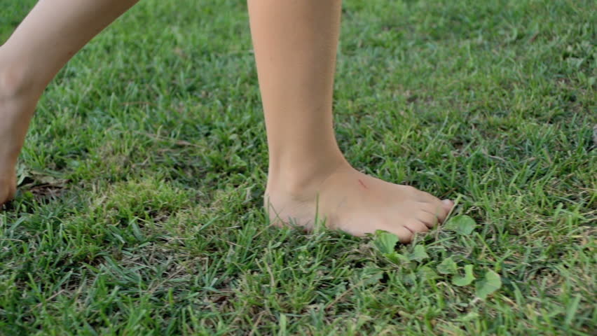 Slow Motion Shot Of A Girls Bare Feet Walking Over Green Grass Field